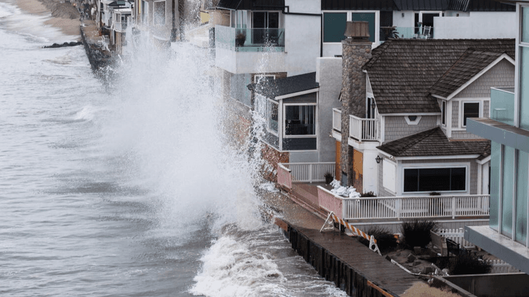 Waves crashing against coastal homes near the edge of the waterline